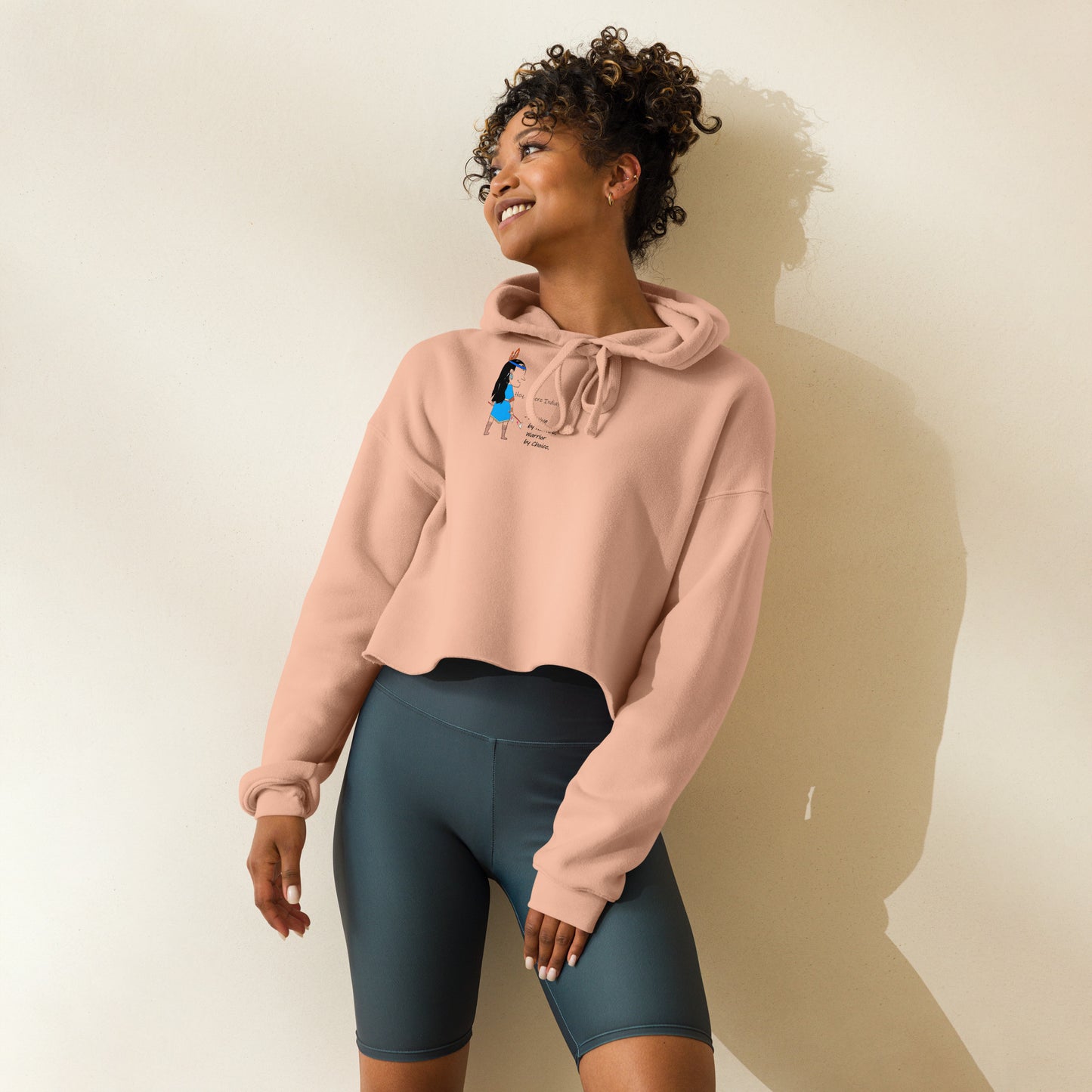 Front view of a lady model wearing a peach cropped hoodie with an American Indian woman graphic design against light on a white background